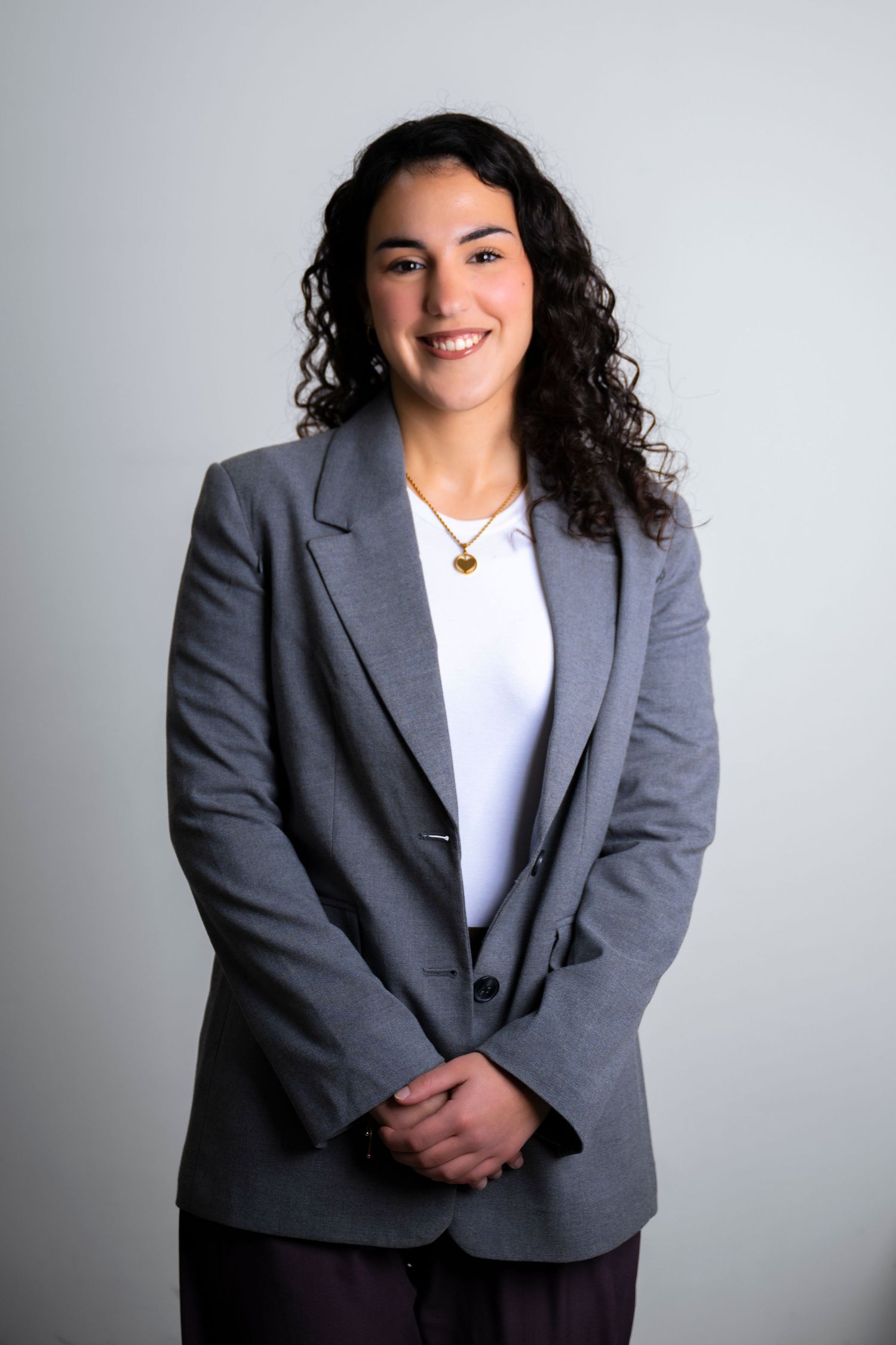 Professional headshot of someone wearing a gray blazer and white top against a light background.