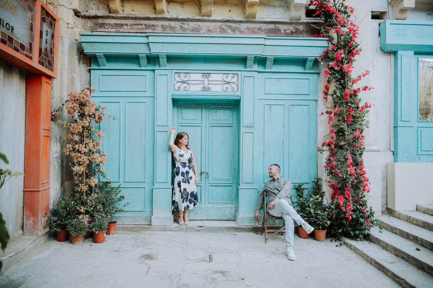 Couple posing in front of a turquoise door with climbing red flowers and lush greenery.