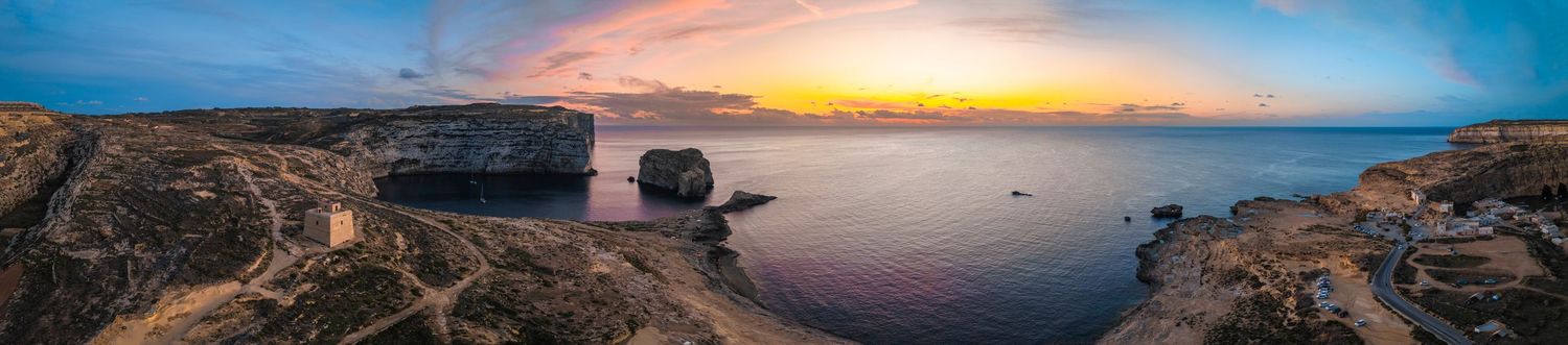 Dramatic sunset panorama over coastal cliffs and Mediterranean seascape with orange sky.