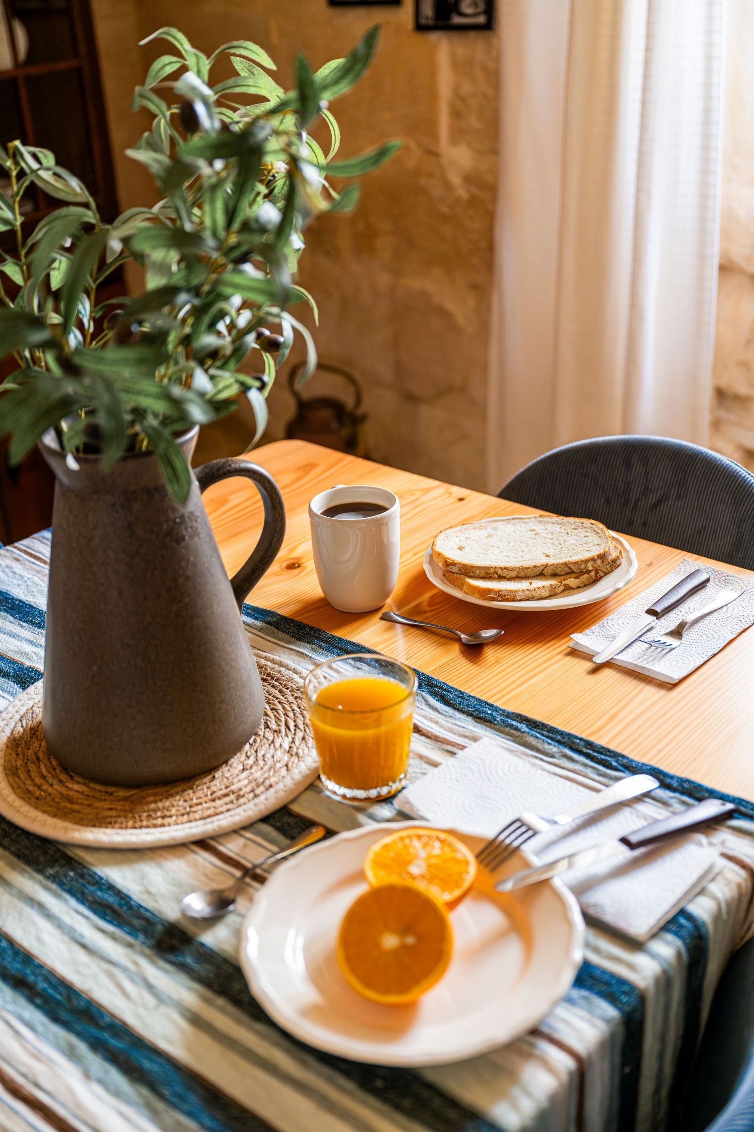 Rustic breakfast setup with coffee, toast and orange slices on a wooden table with striped cloth.