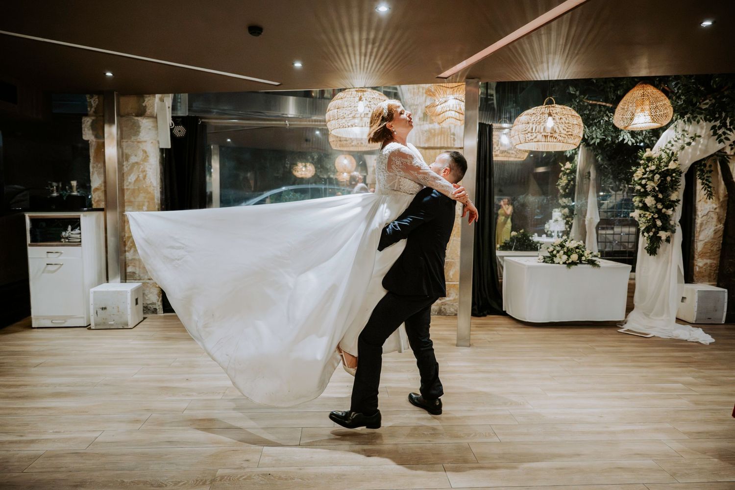Groom lifting bride in white gown during romantic first dance at elegant wedding reception venue.