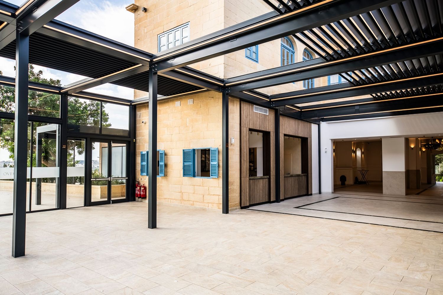 Modern covered walkway with black metal beams and wooden slats creating geometric patterns and shadows.