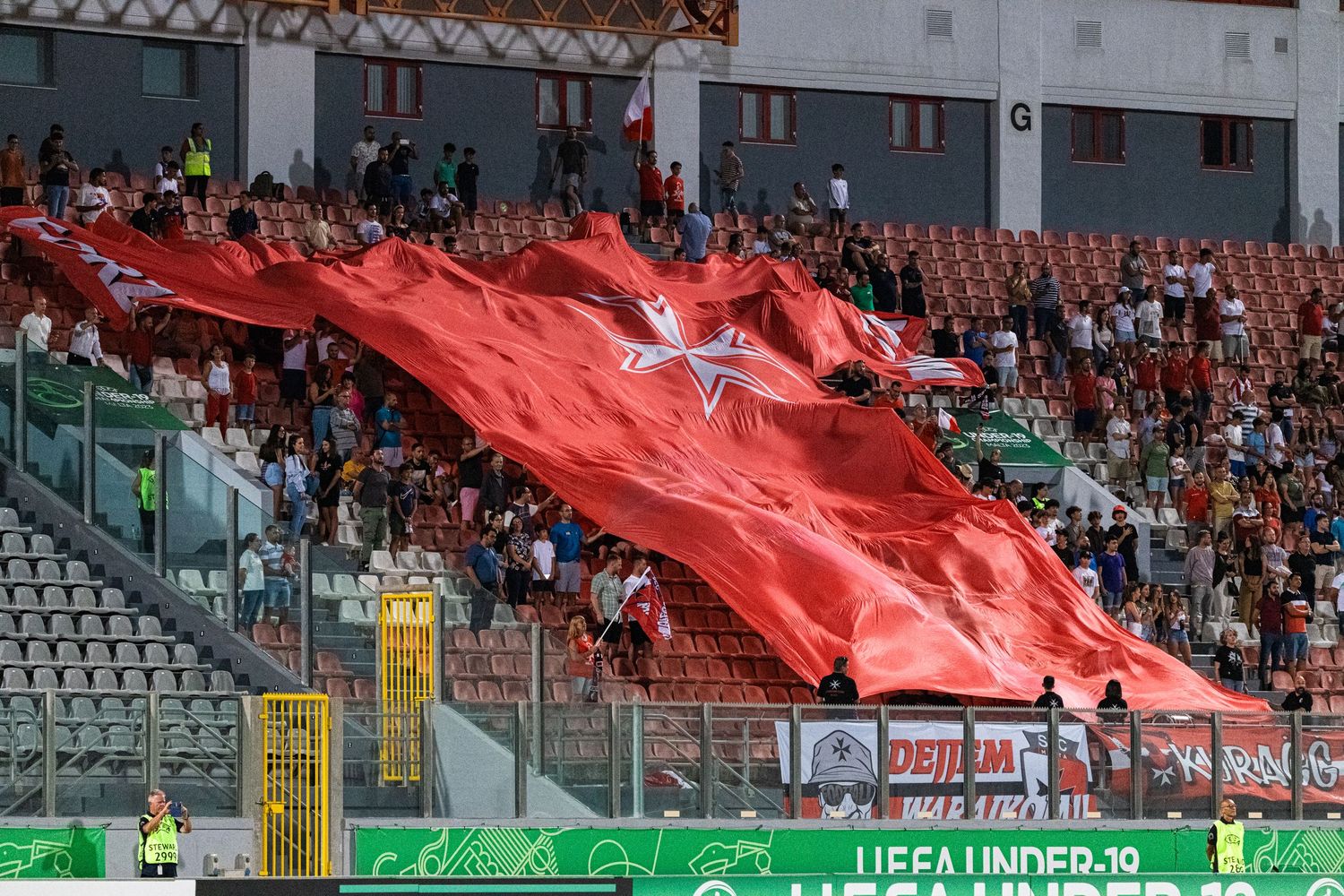Stadium stands with red banners and spectators during a soccer match.