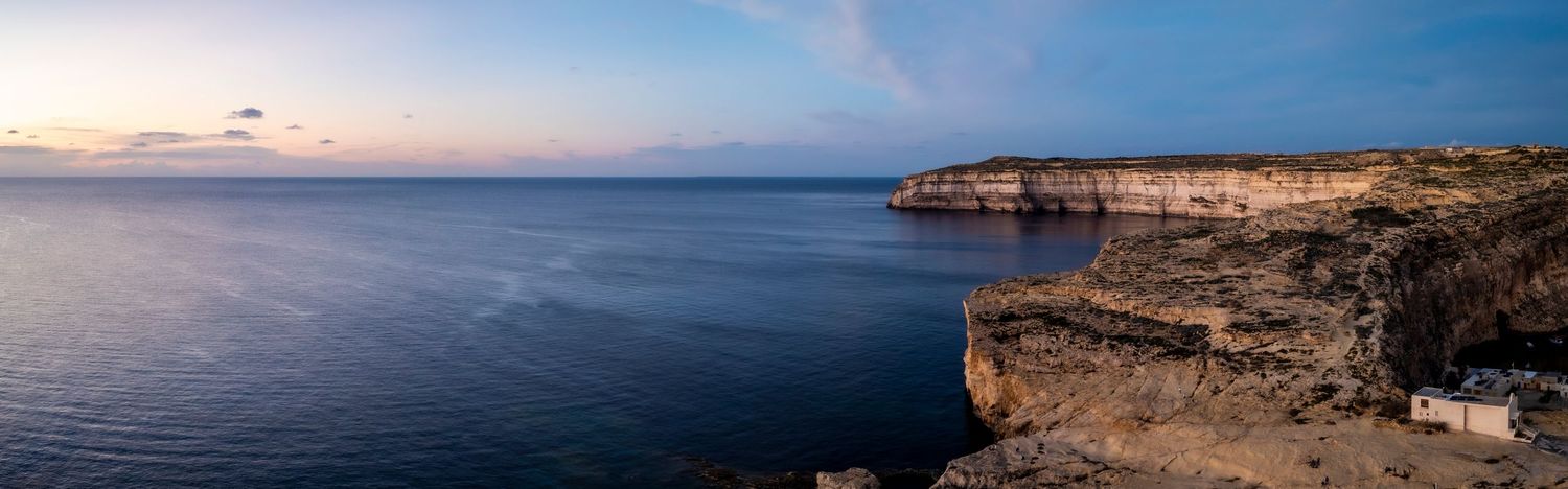 Panoramic seascape showing rugged coastline and rocky cliffs against blue horizon.