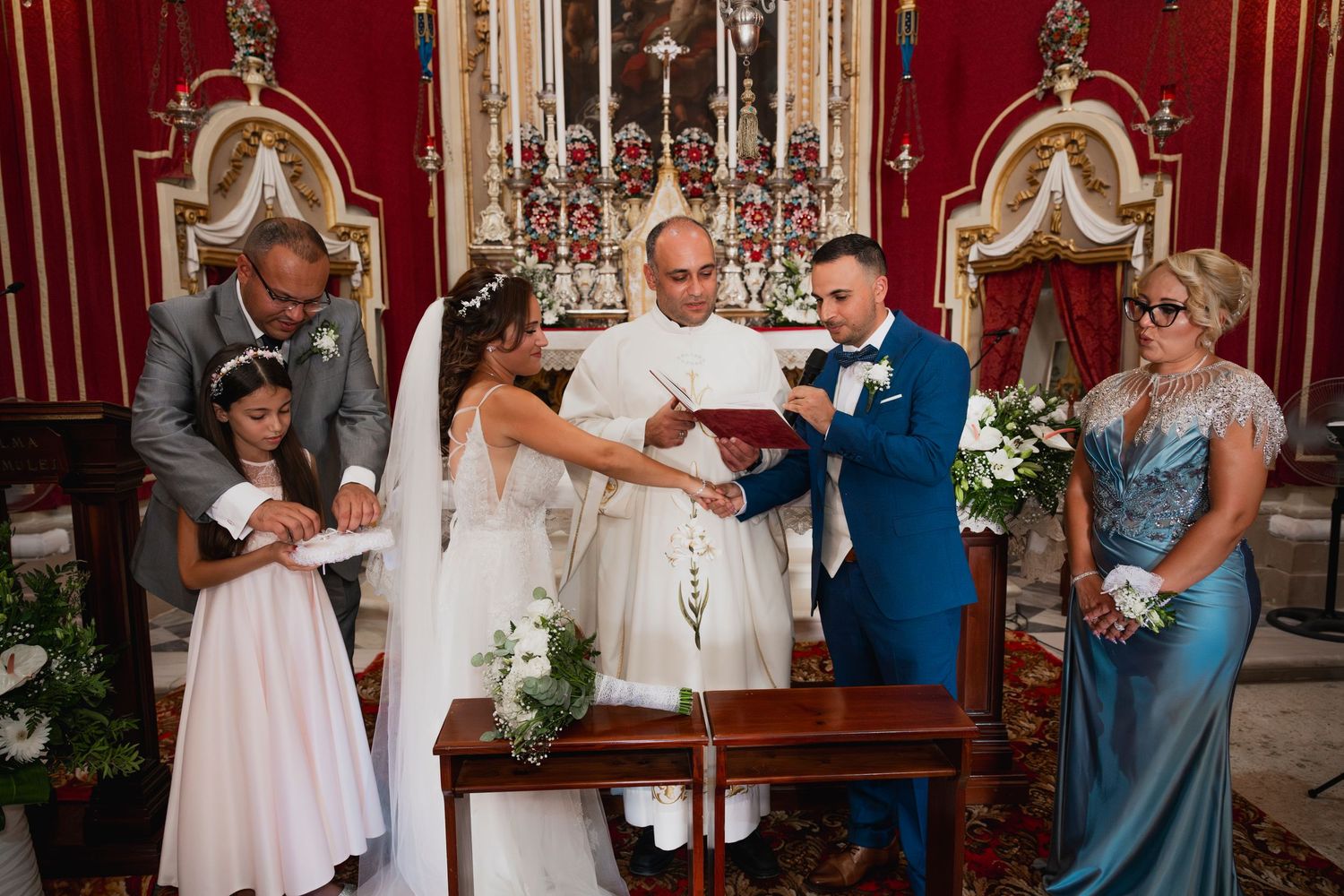 Wedding ceremony in a grand red room with ornate decor and guests in attendance.