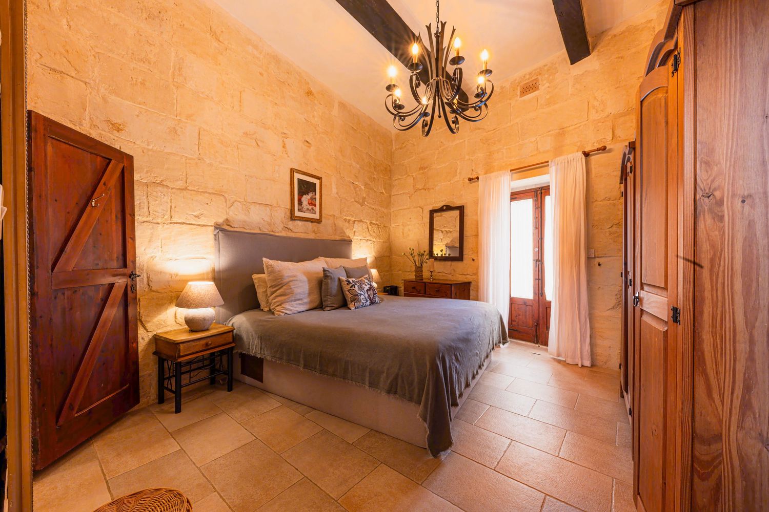 Rustic bedroom with stone walls, wooden beams, and elegant gray bedding.