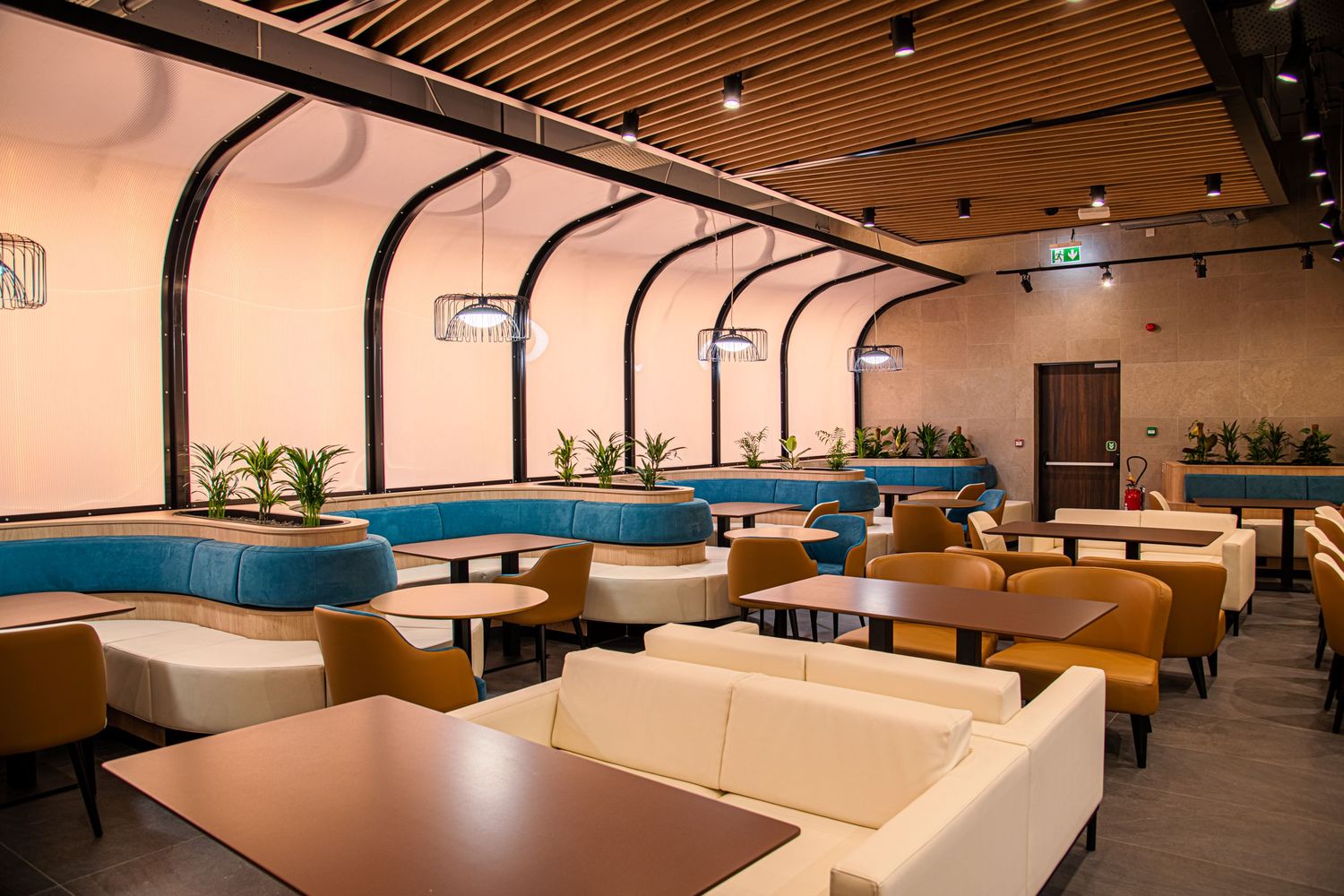 Modern cafeteria space with wooden ceiling panels and built-in seating areas.