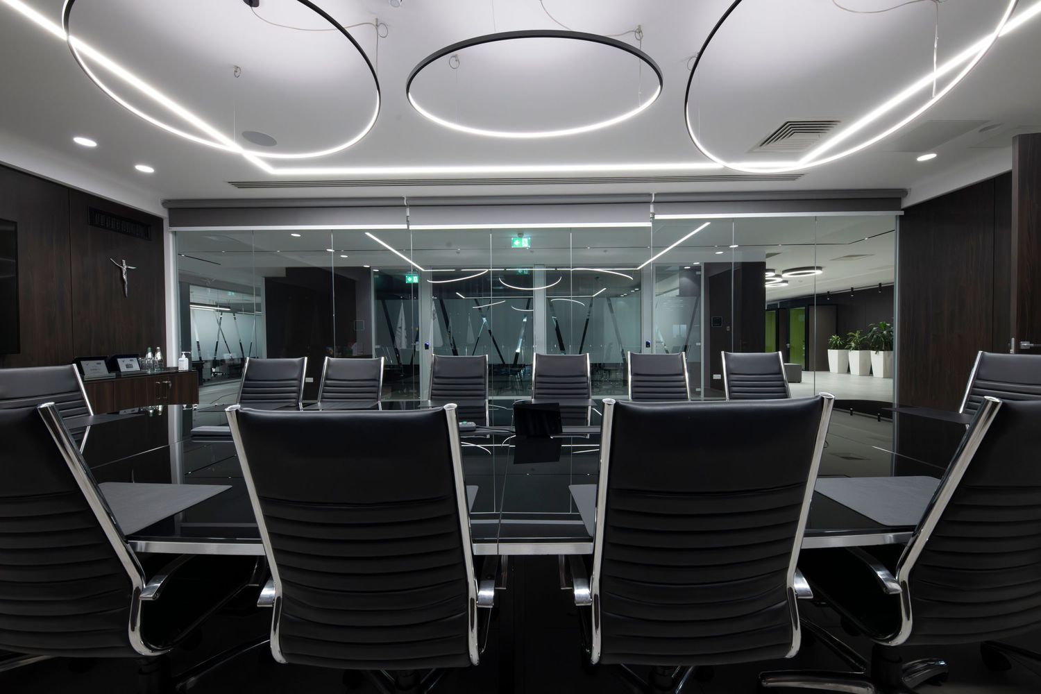Corporate boardroom with curved LED ceiling lights and black leather chairs around a large conference table.