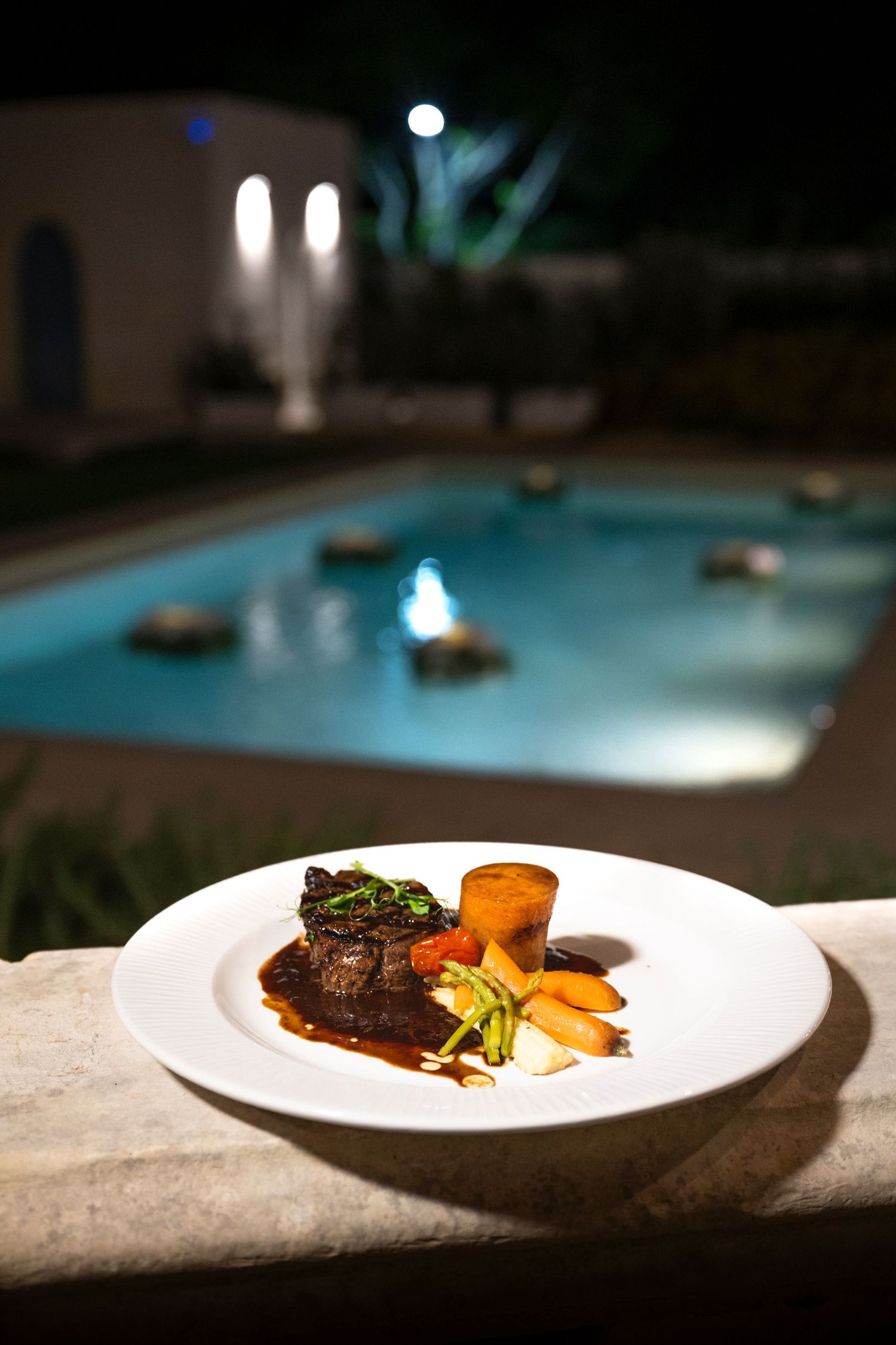 Poolside fine dining with beautifully plated dishes illuminated in evening light.