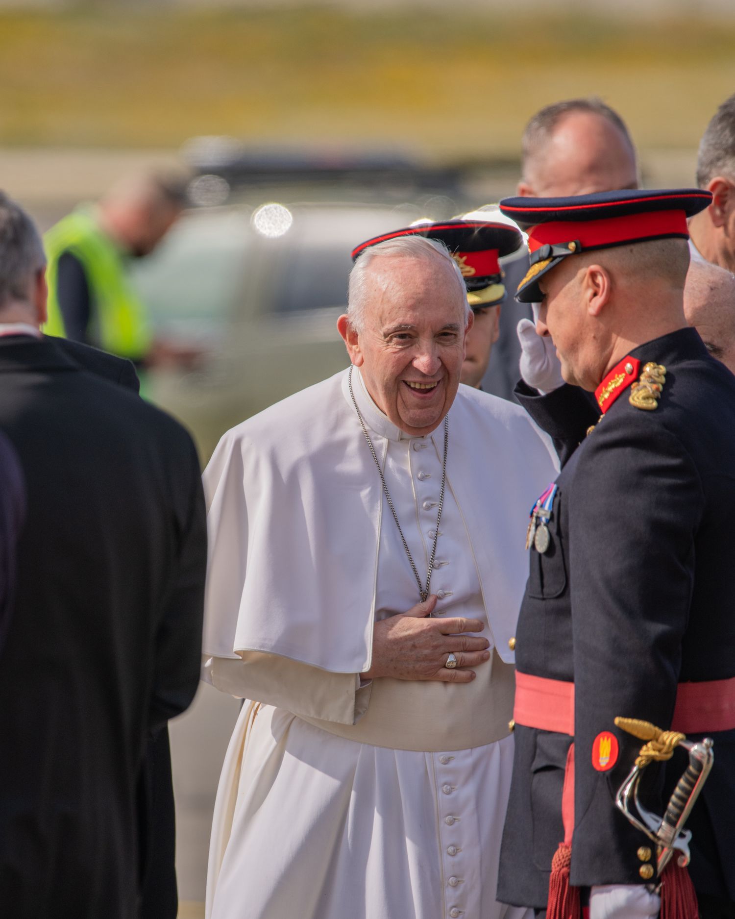 Religious leader in white robes greets military official during outdoor ceremony.