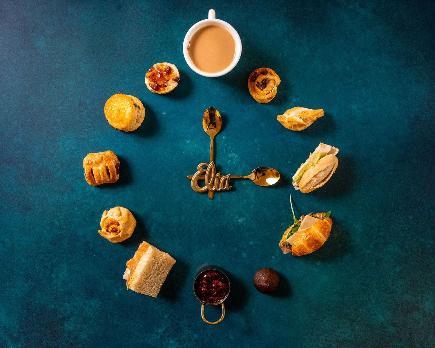 Assorted pastries and coffee arranged on a dark blue background in flat lay composition.