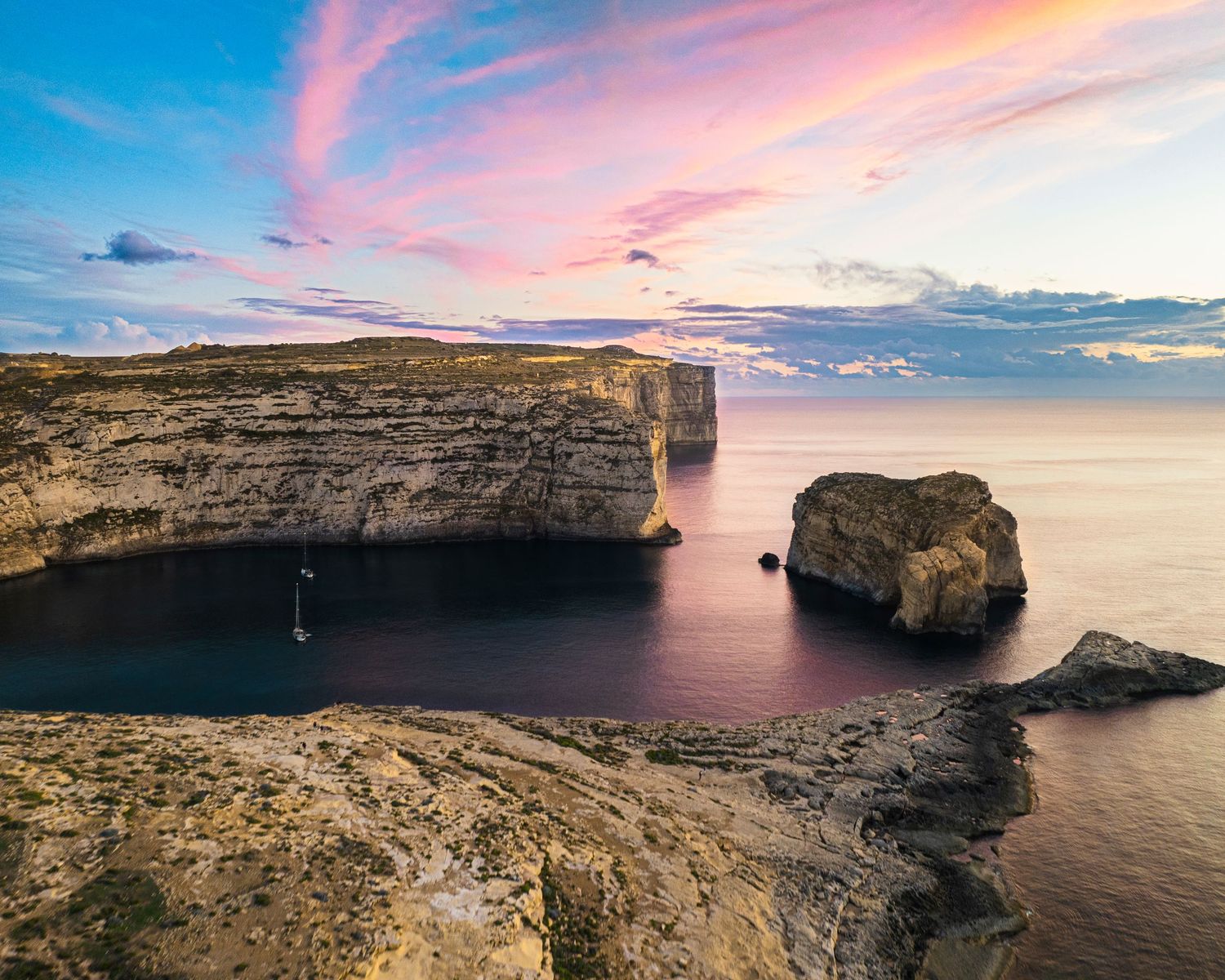 Stunning coastal panorama featuring limestone cliffs and pink sunset skies over Mediterranean waters.