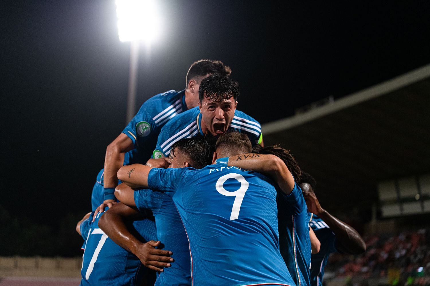 Soccer team in blue uniforms celebrating under stadium lights at night.