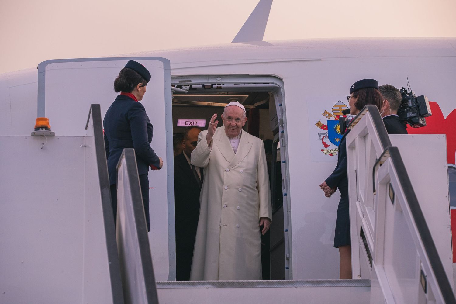 Religious leader in white robes boards an aircraft with assistance from officials.
