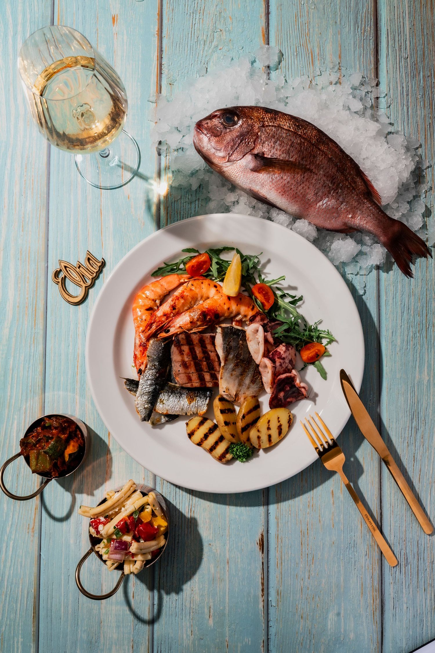 Fresh seafood platter with grilled fish and prawns on white plates against blue wooden background.