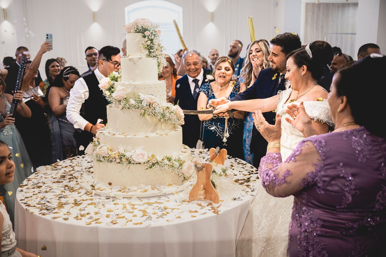 Wedding celebration scene with confetti flying as guests celebrate around a decorated cake.