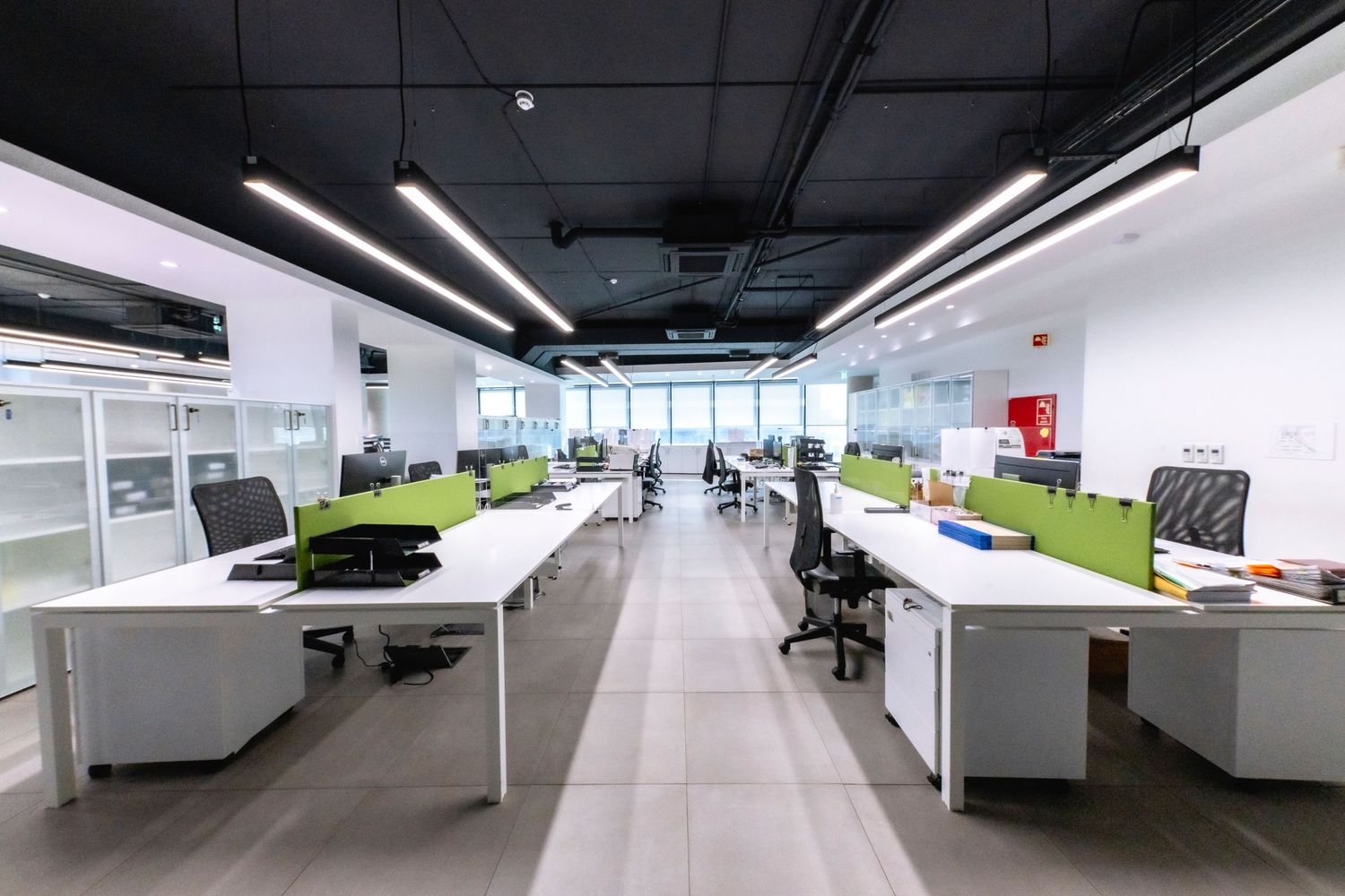Open plan office space with minimalist white workstations and large windows.