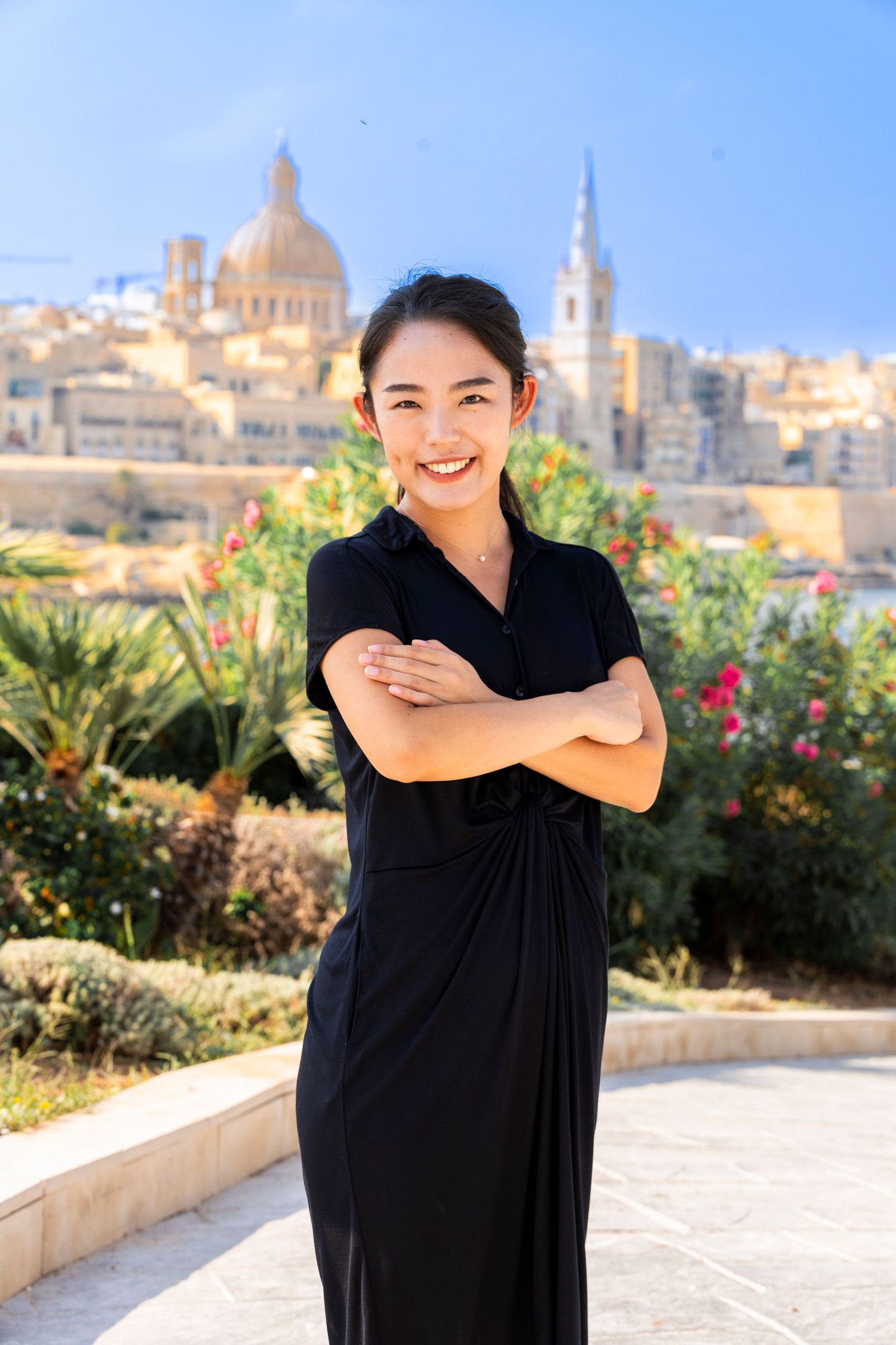 Person in black outfit posing against scenic city backdrop with historic architecture.