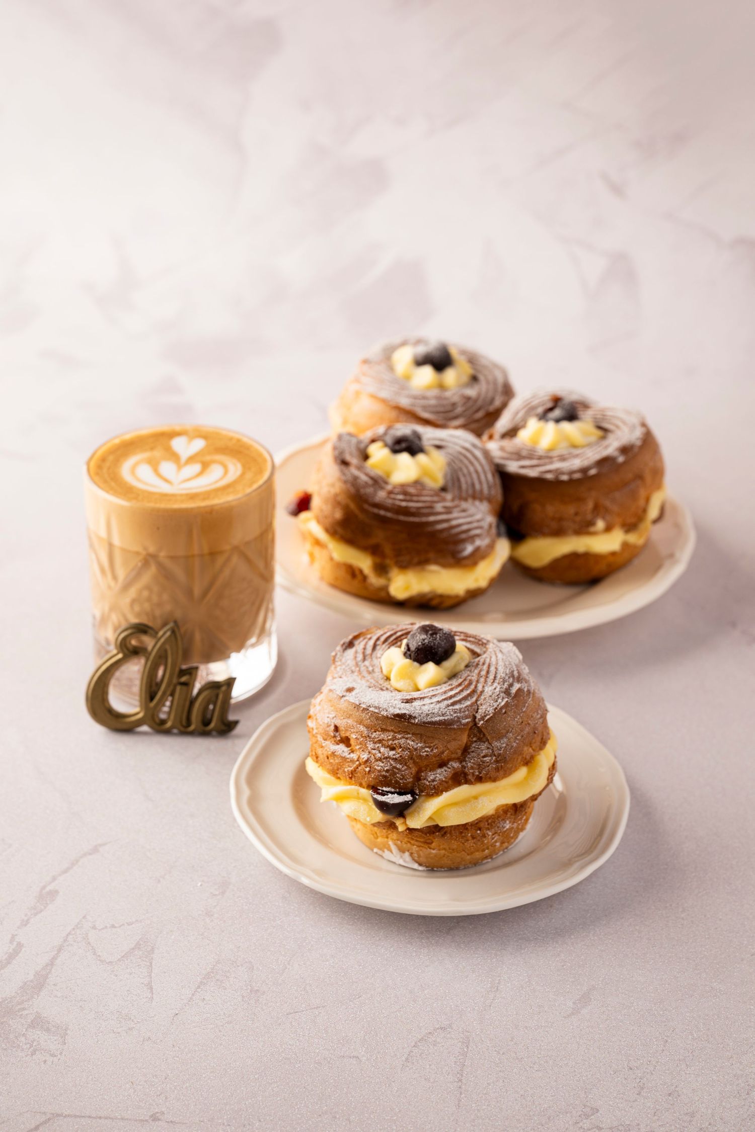 Artisanal pastries with chocolate and cream filling arranged on white plates against a light marble background.
