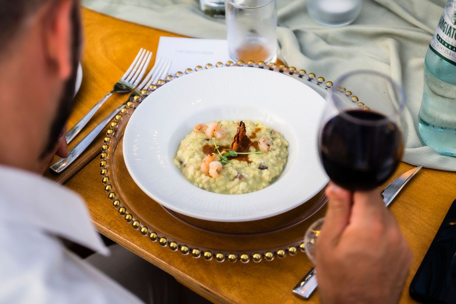 Elegant plated dishes and wine glasses on a formal dining table with gold charger plates.