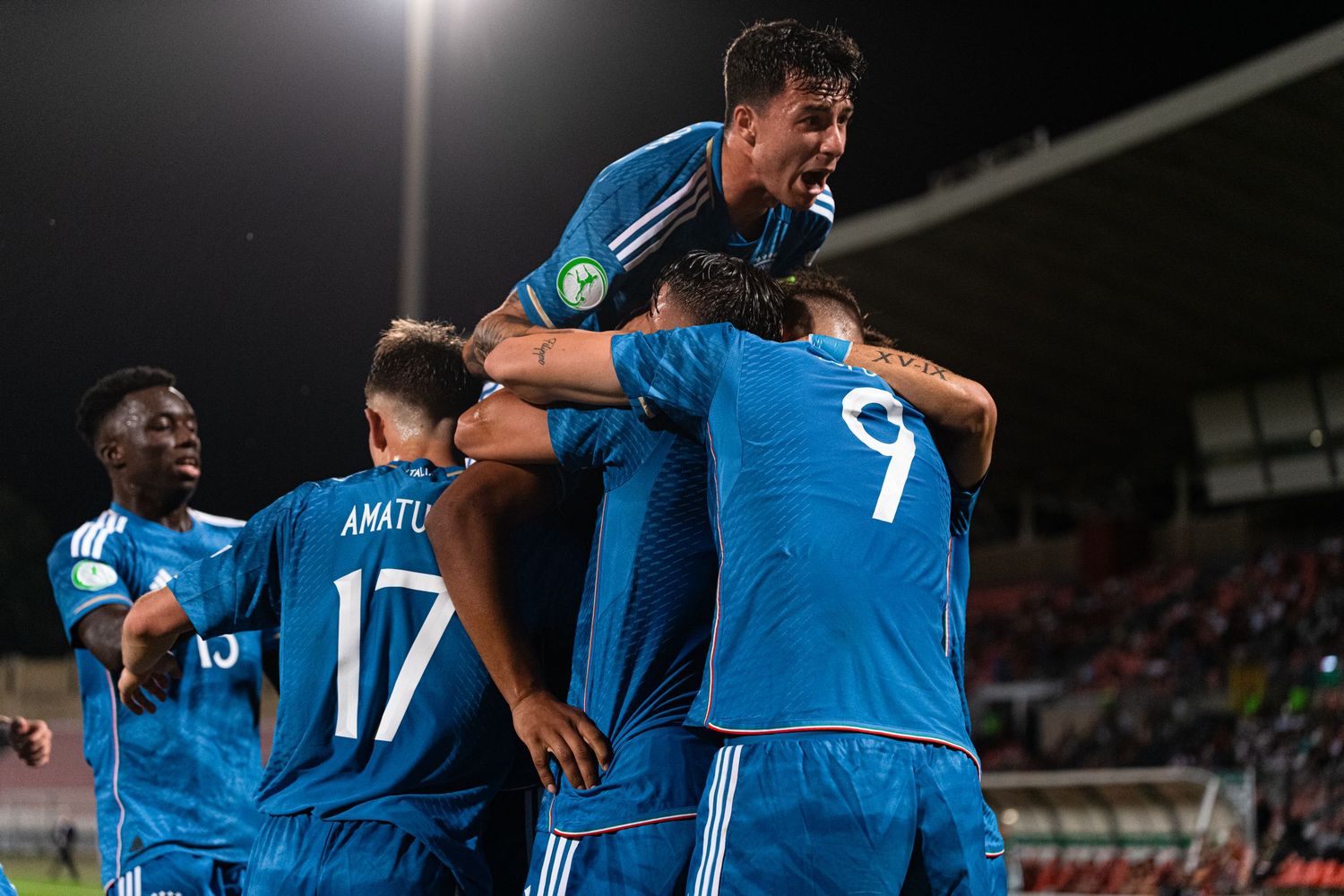 Soccer team members in blue uniforms huddle together during game celebration.