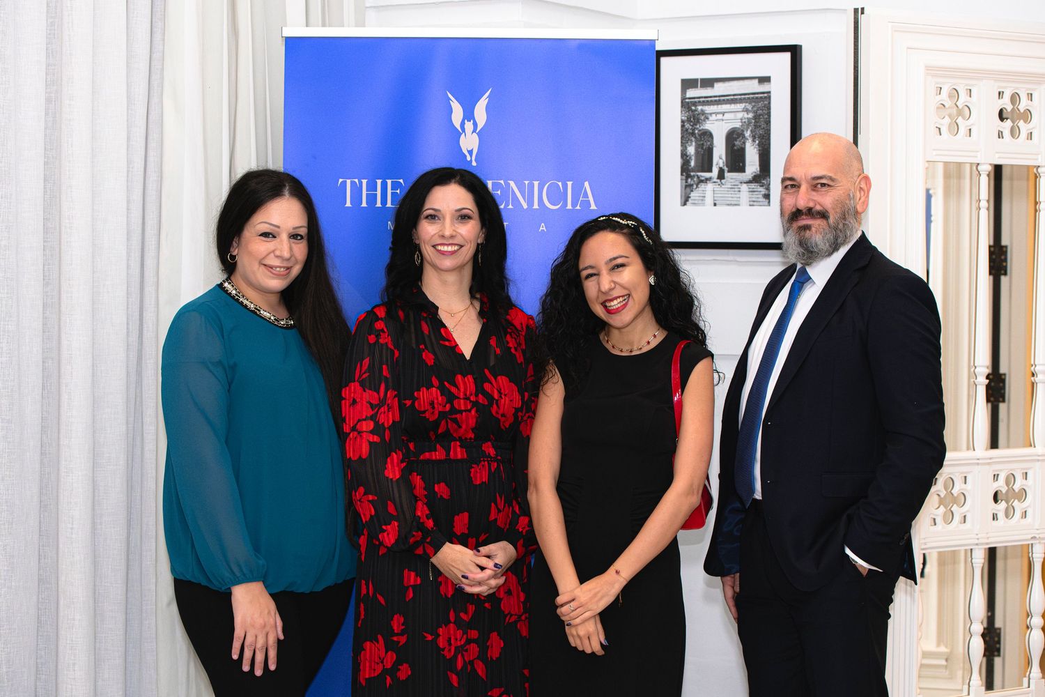Group photo of four professionals against blue Phoenicia branded backdrop at formal event.