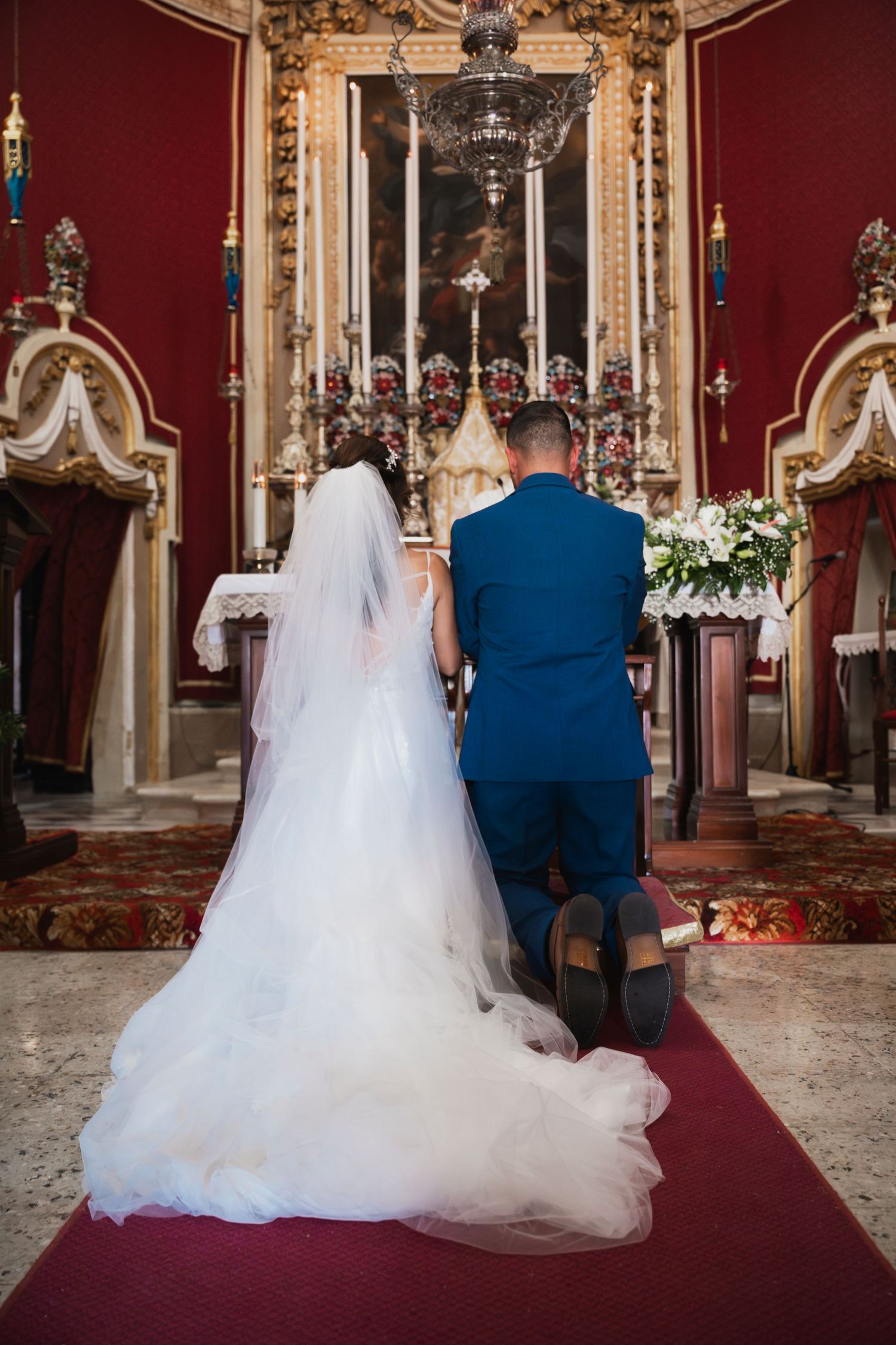 Couple seated at altar in ornate red church during wedding ceremony.