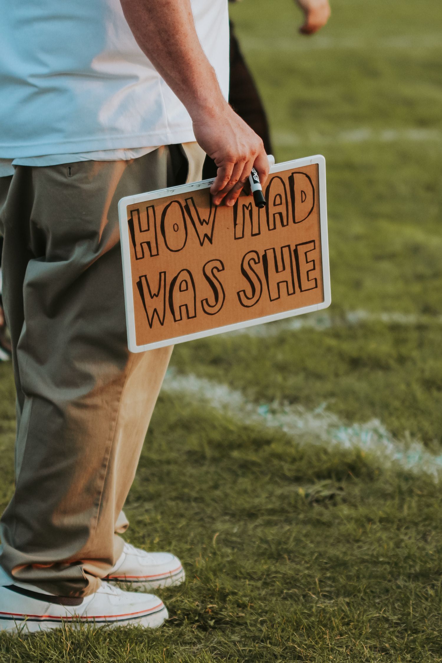 Person in khaki pants and light blue shirt holds brown signs on a grassy football field.