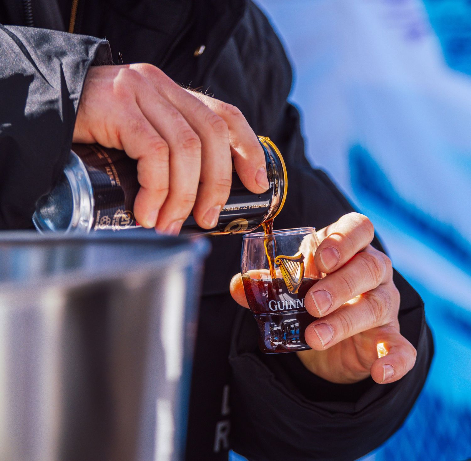 Person pouring Guinness beer into a shot glass outdoors at an event.