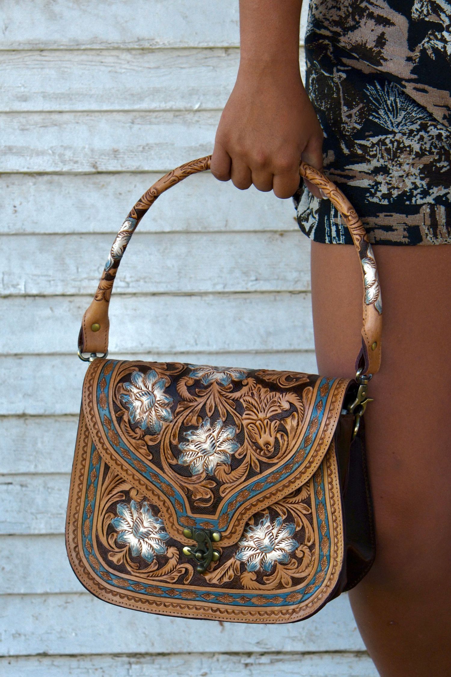 Vintage-style tooled leather handbag with ornate floral design and metallic accents.