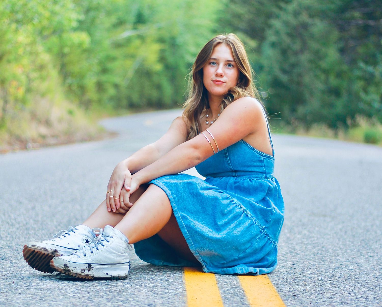 Person in blue dress sits casually on a rural road with yellow lines.