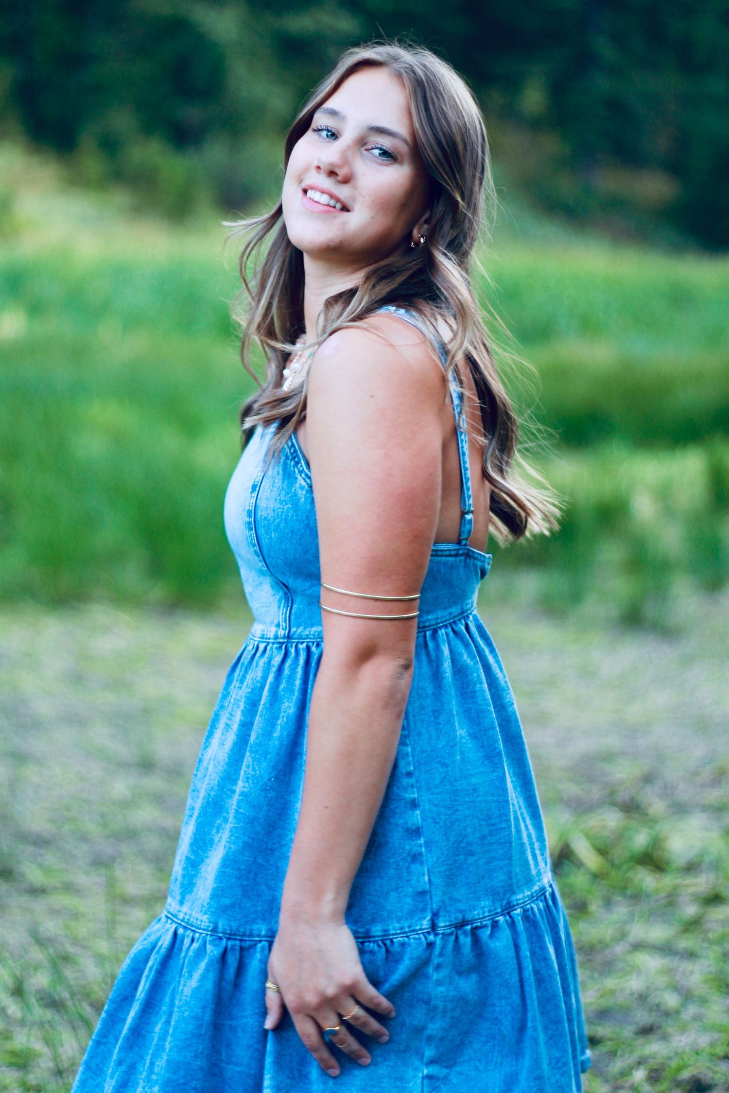 Person in blue tiered dress twirls joyfully in a green summer meadow.