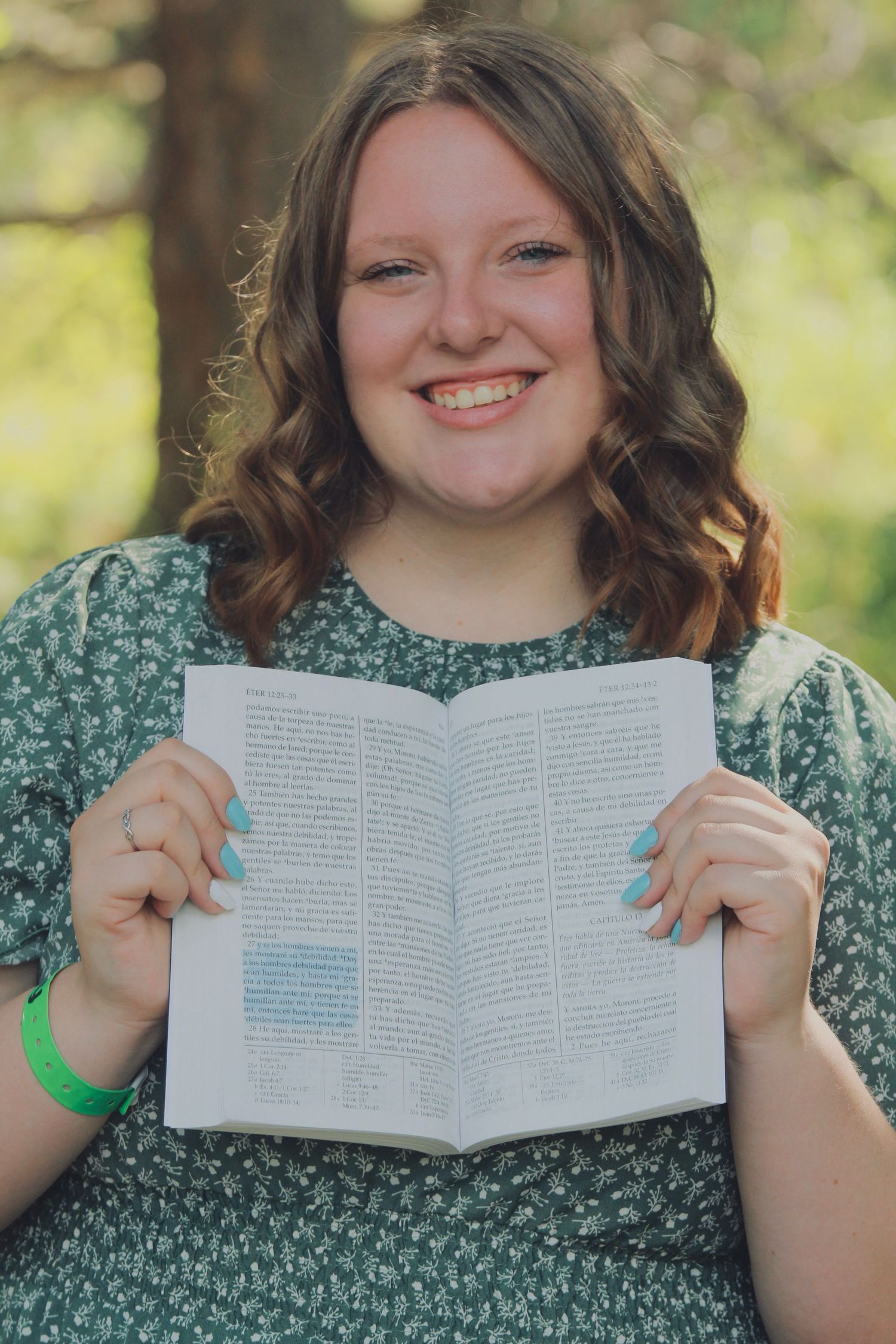 Person in green floral dress holds open book while sitting outdoors.