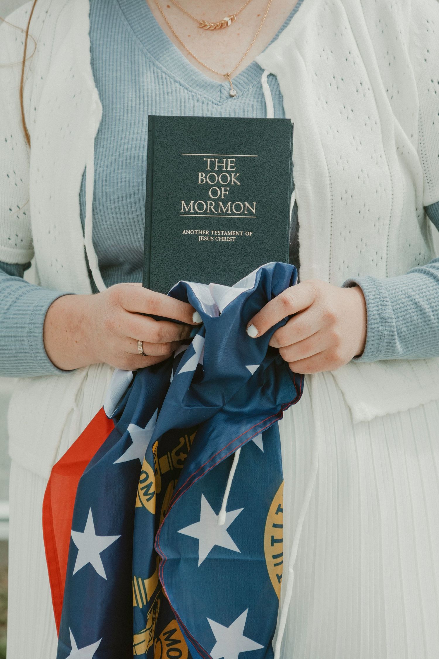 Person holding The Book of Mormon with an American flag draped over it.