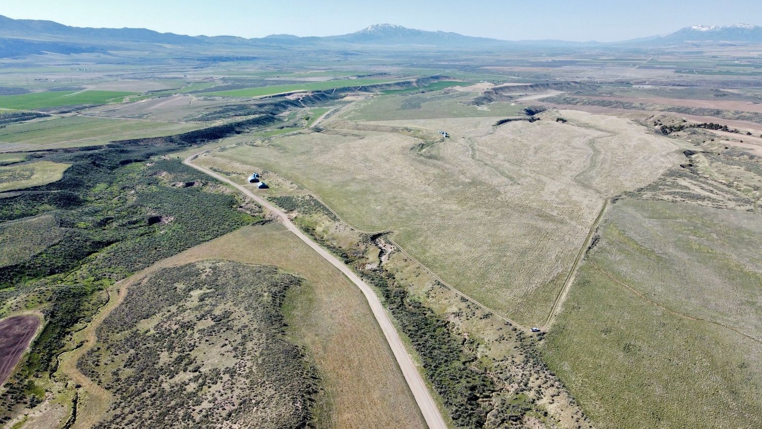 Drone shot of winding road through rugged terrain with mountains in the background.