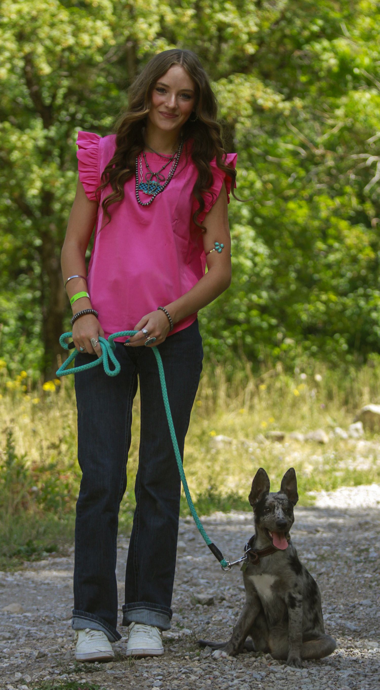 Person in pink shirt walking a small black and grey dog on gravel path.