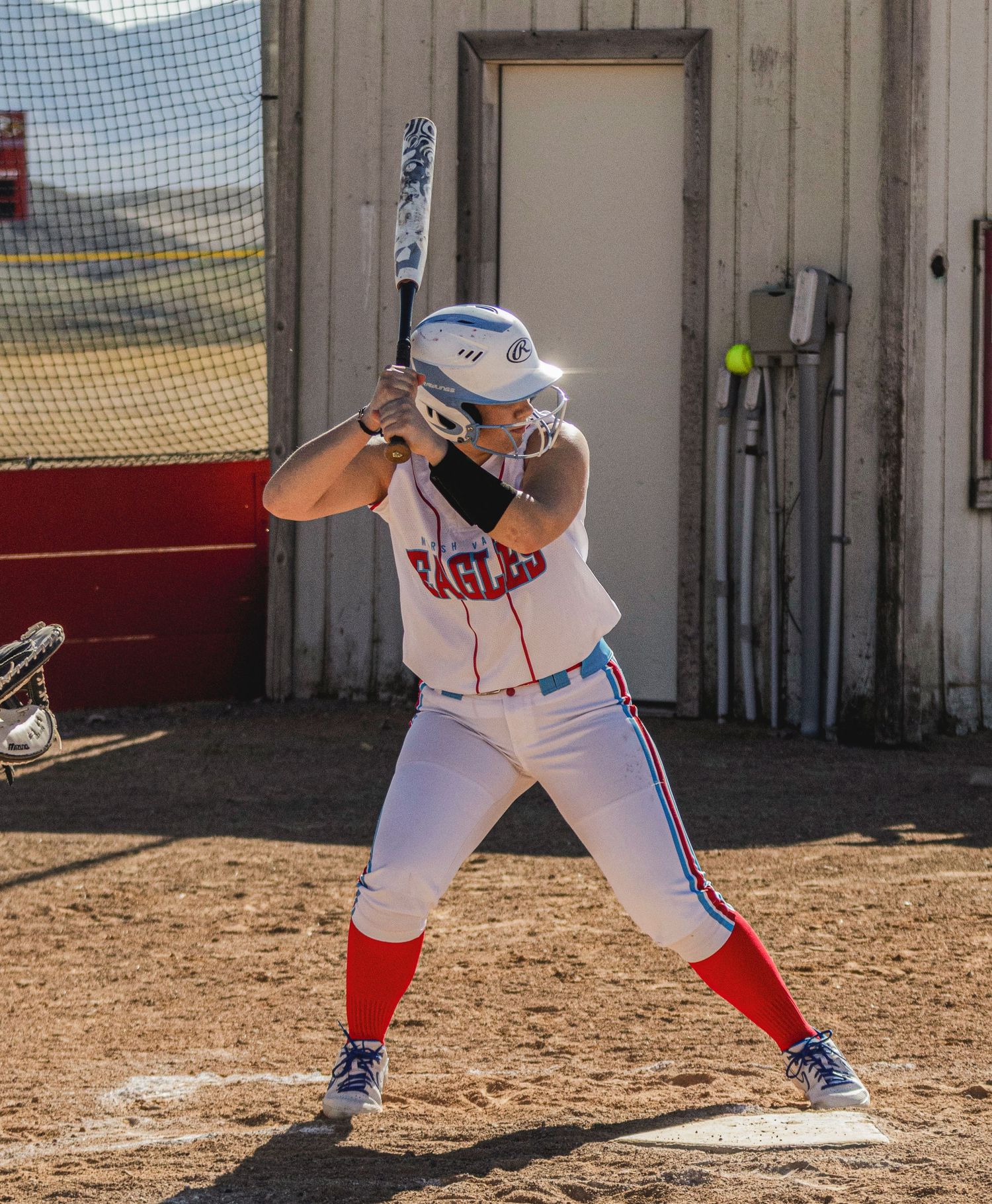 Female softball player in white and red Eagles uniform stands ready at bat on a dirt field.