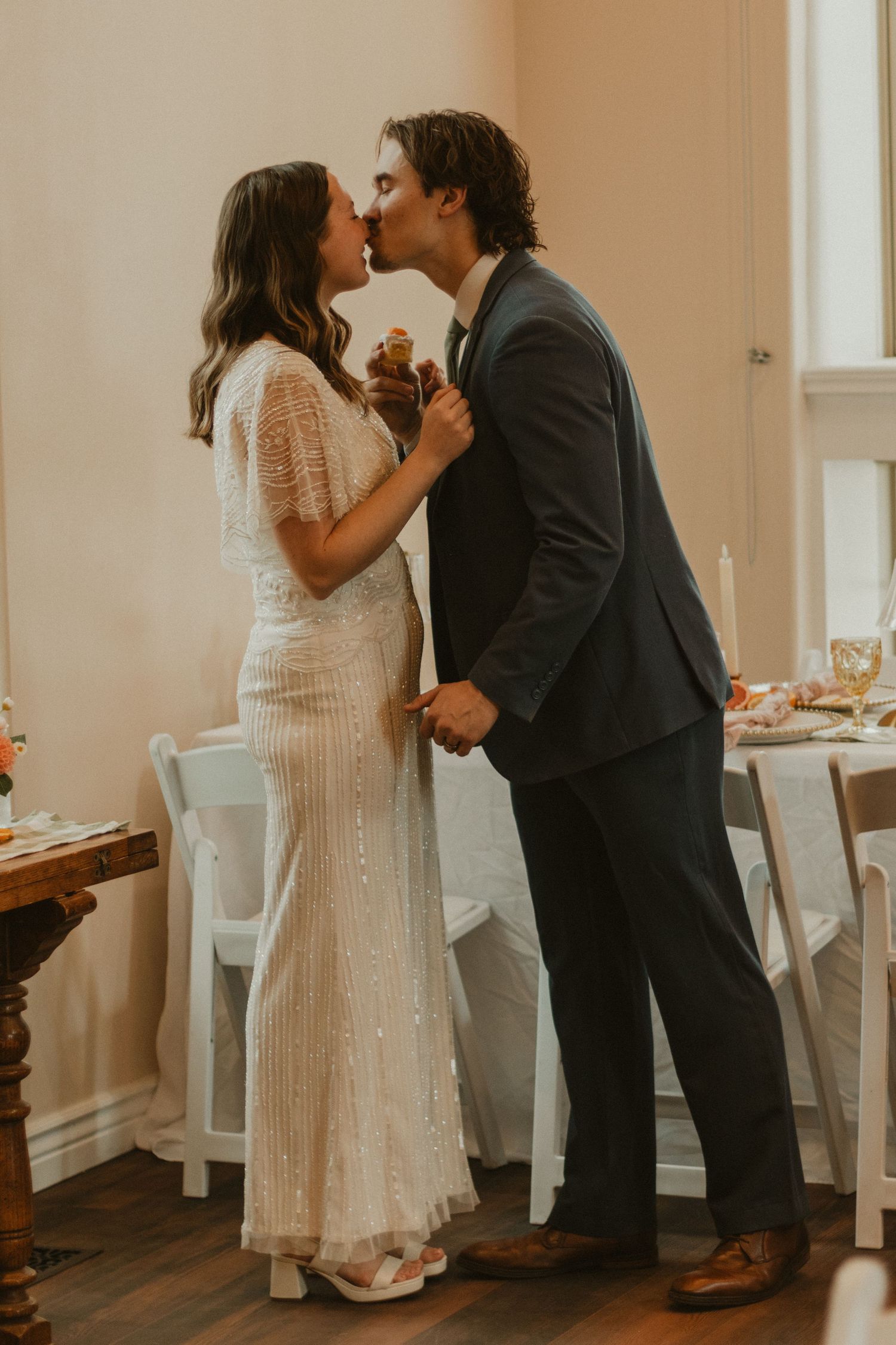 A couple shares their first dance together in a bright indoor venue with white walls and hardwood floors.