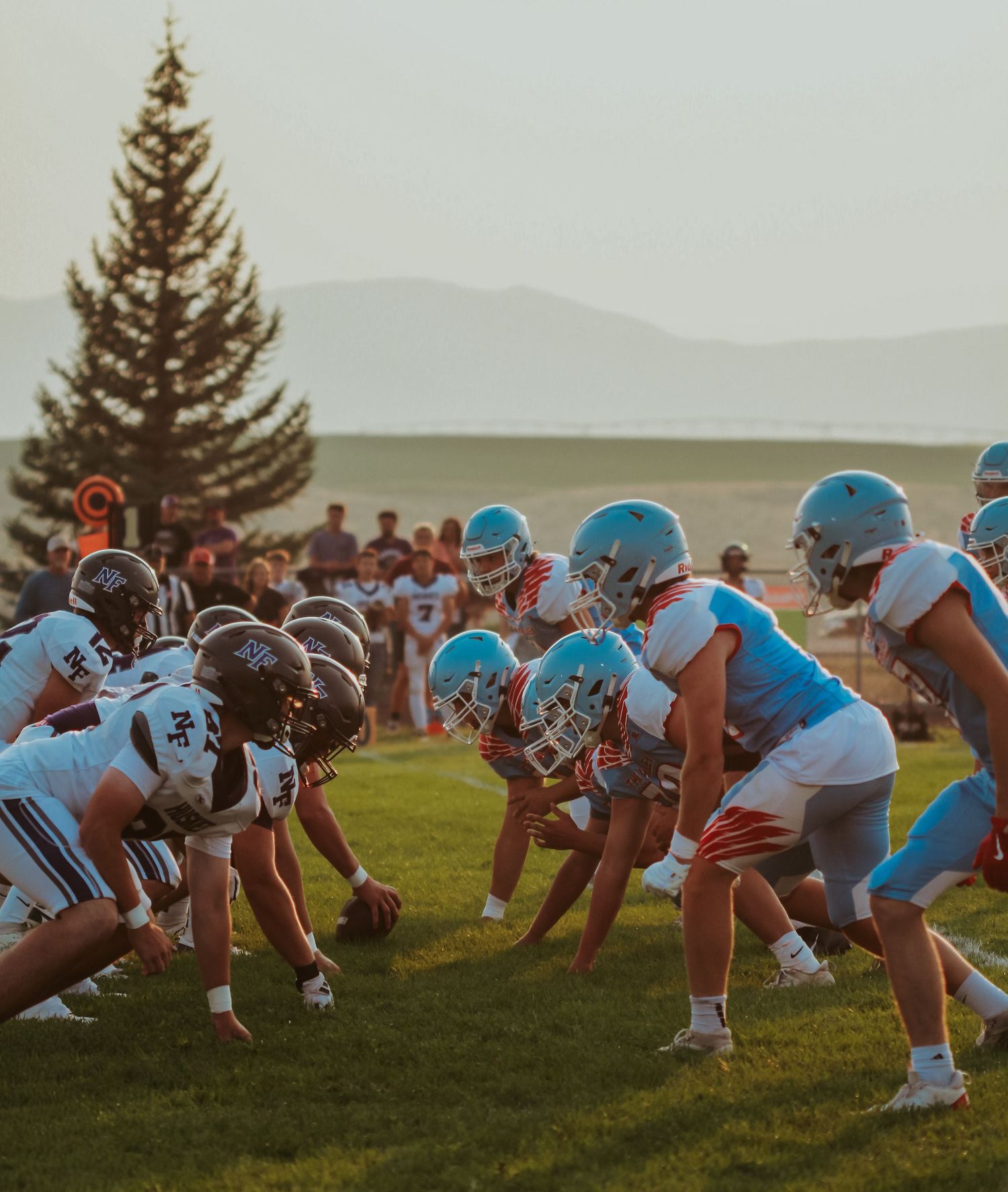 Two football teams face off at the line of scrimmage during a sunset game.