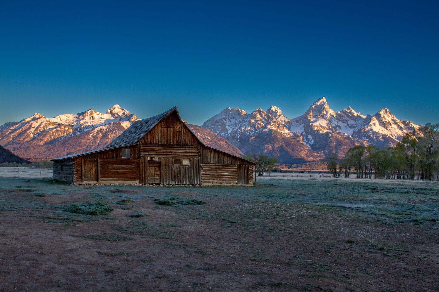 Historic wooden barn at Mormon Row with snow-capped Grand Teton mountains at sunrise in Wyoming.