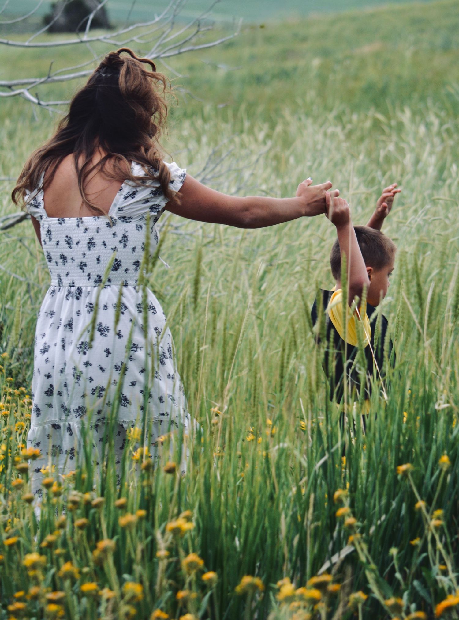 Dancing and twirling through a meadow of yellow wildflowers and tall grass on a sunny day.