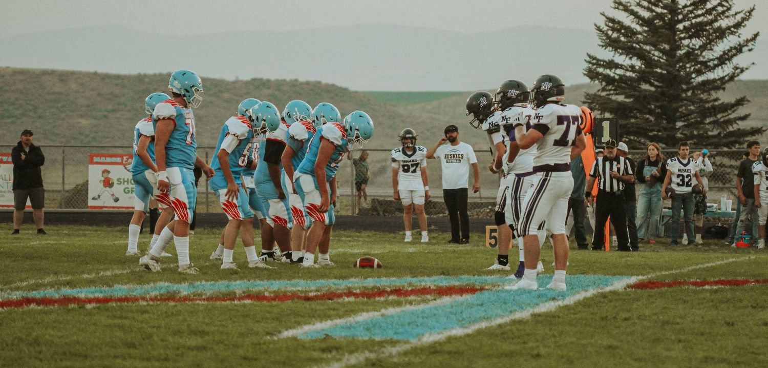 Wide view of football field with players and spectators during evening game.