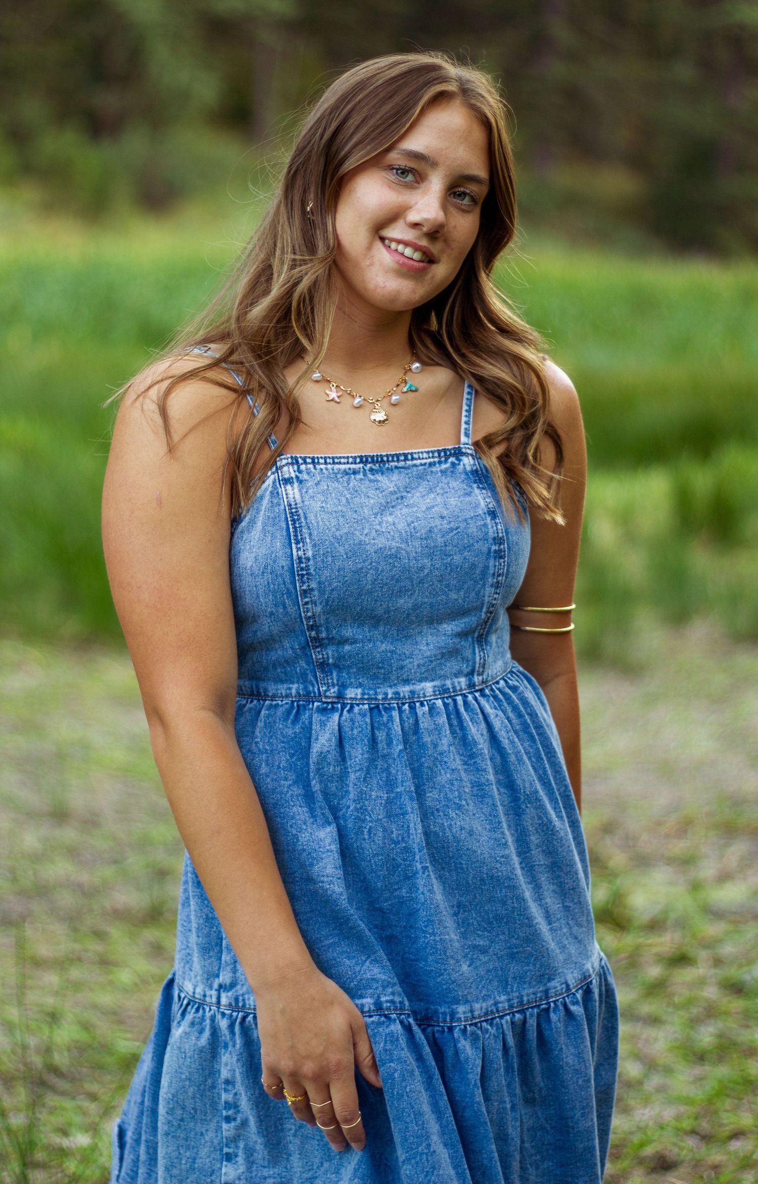 Person wearing denim tiered dress poses outdoors in natural setting.