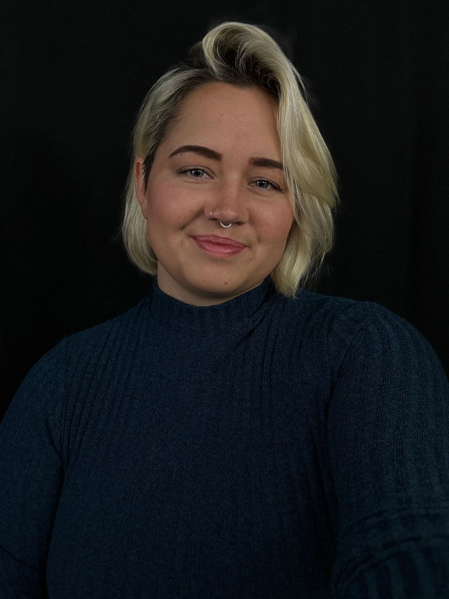 Portrait of person in navy turtleneck sweater against black background.