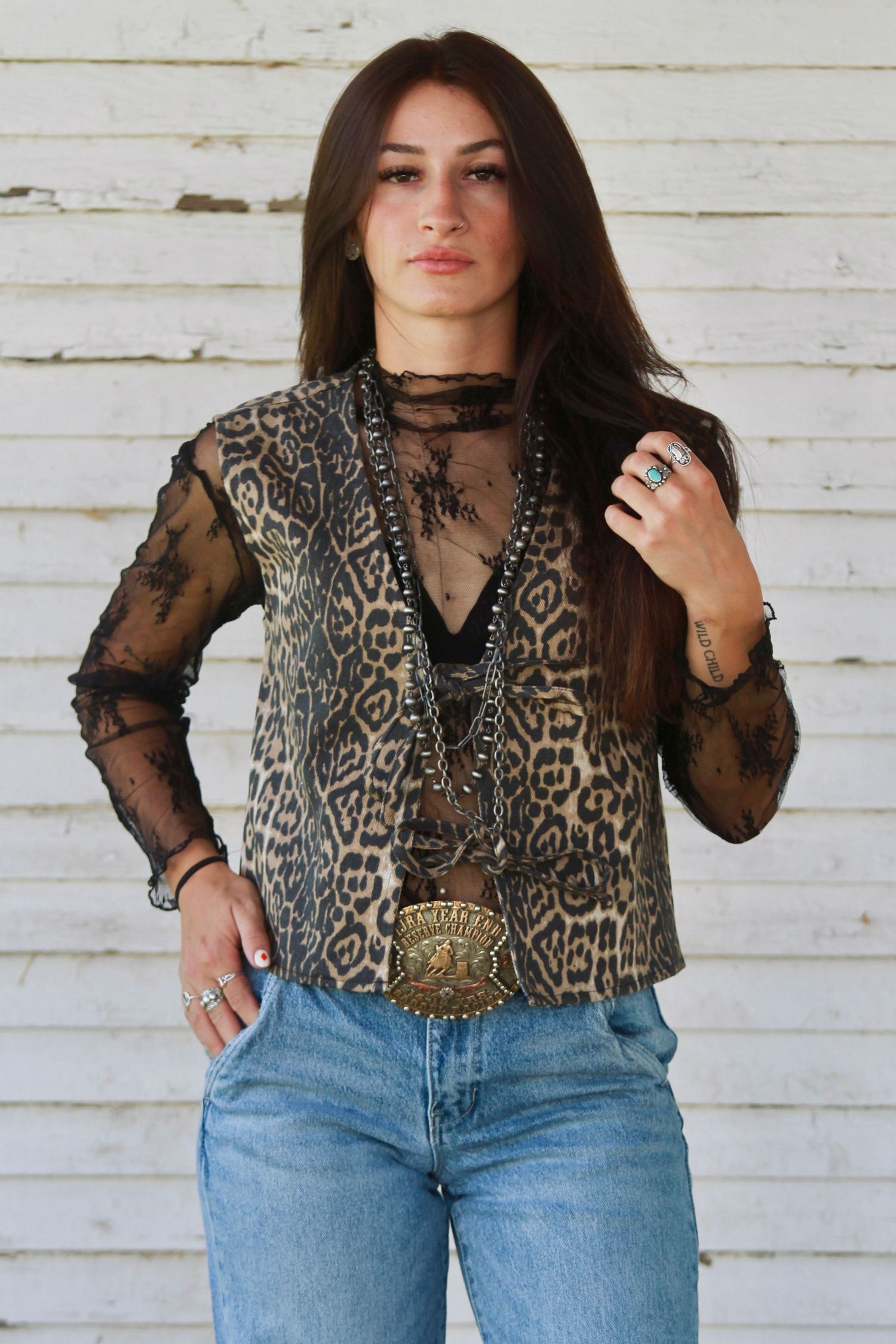 Stylish leopard print blouse with sheer black sleeves paired with light wash denim jeans against white wall background.