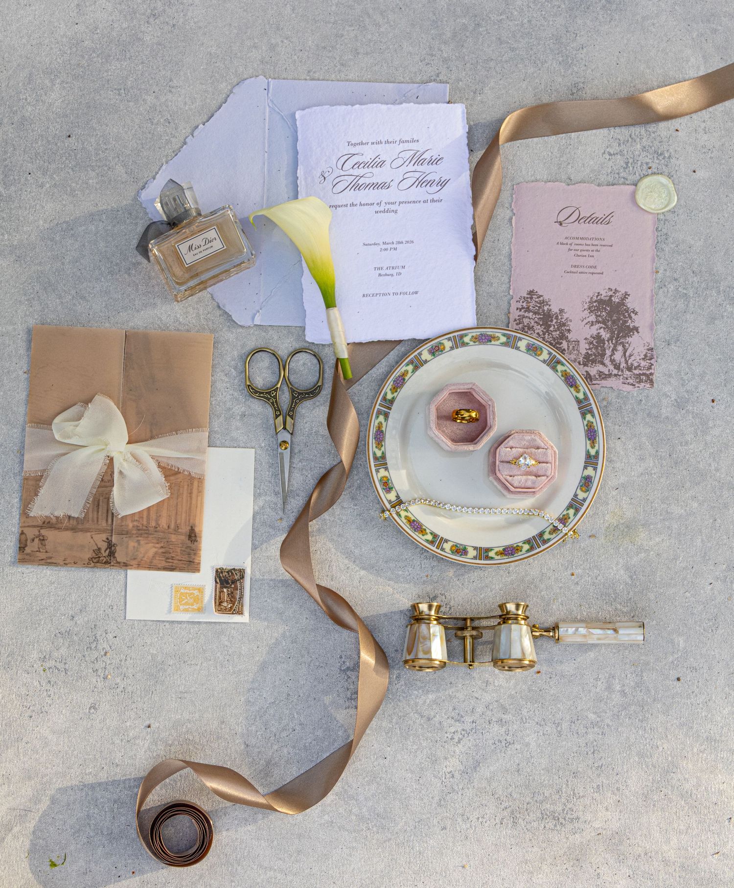 Elegant wedding flat lay with invitations, vintage scissors, gold ribbon, opera glasses, ring box, and floral details.
