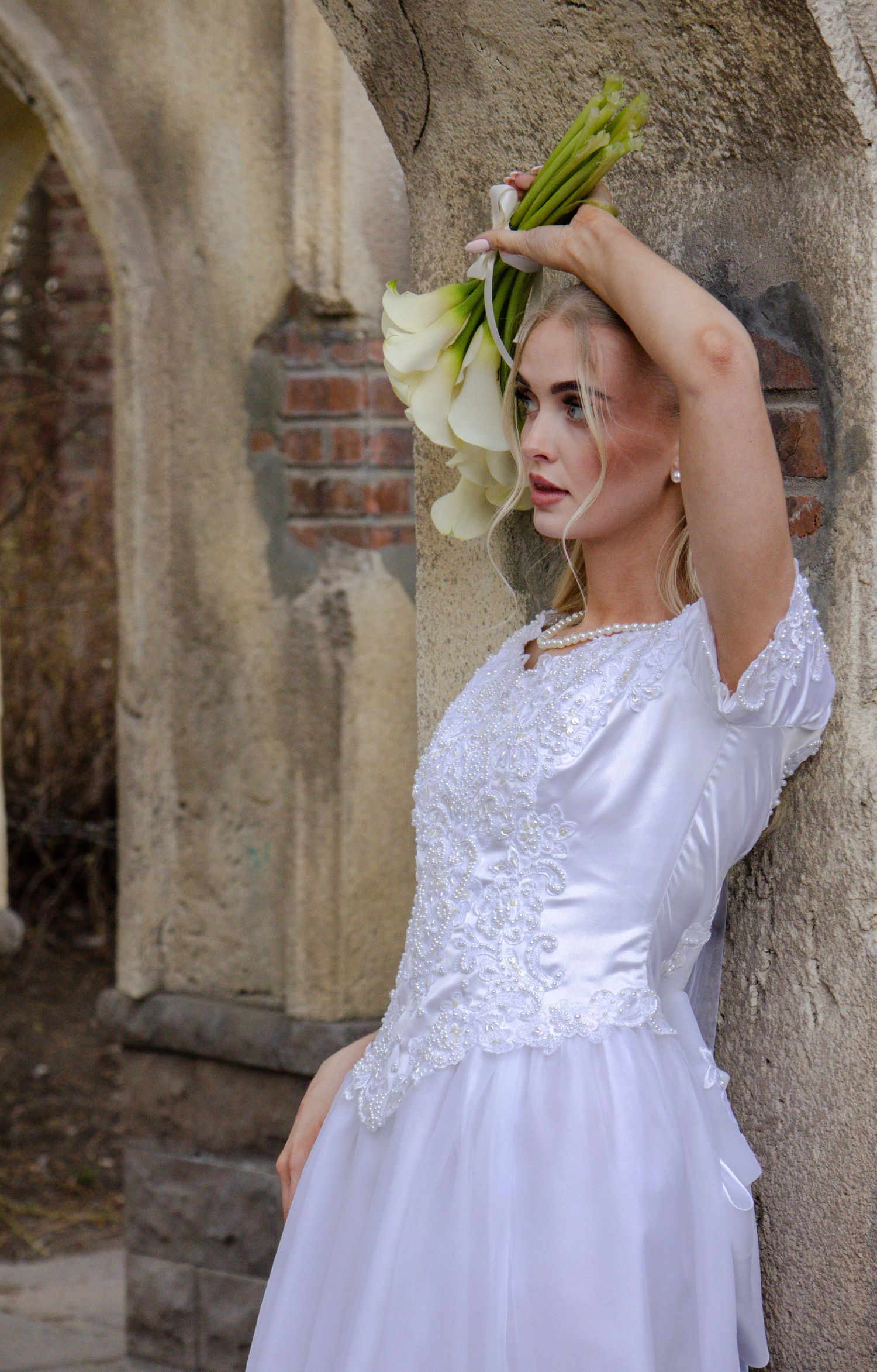 A child in a white lace dress twirls and plays with a large white flower against a stone wall backdrop.