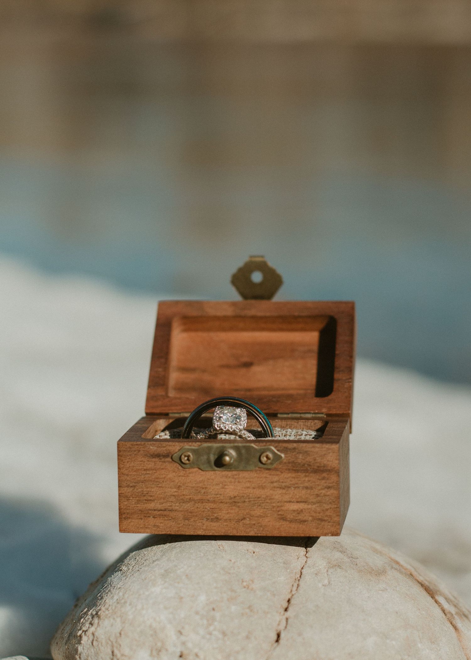 A wooden ring box opens progressively to reveal a diamond engagement ring nestled inside on a textured white surface.