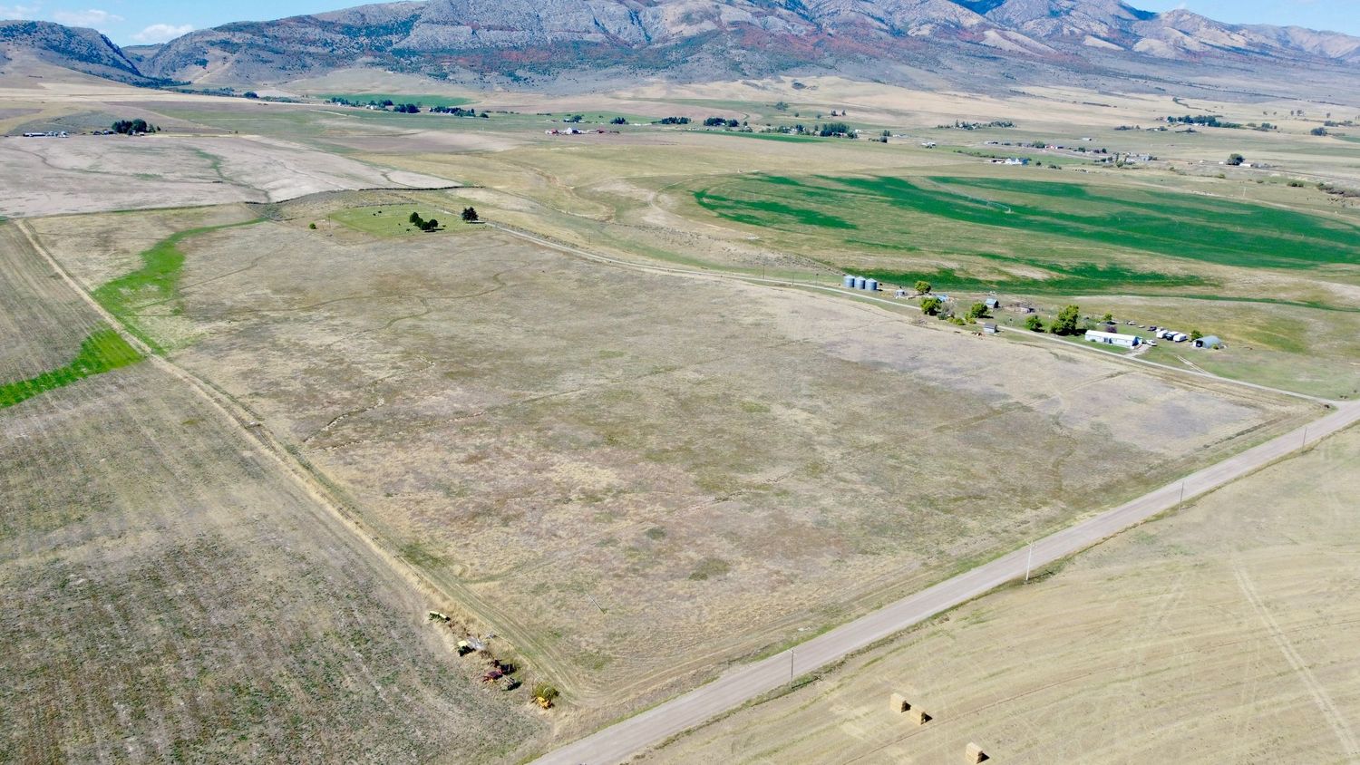 Aerial view of rural farmland with green patches surrounded by mountains in the distance.