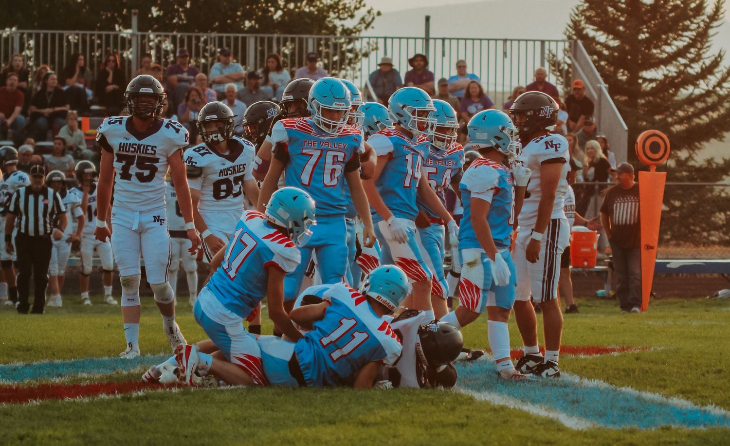 Football team in light blue uniforms huddles on the sideline during a game.